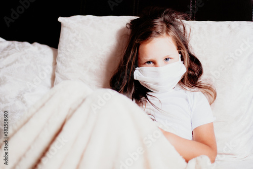 girl sitting in a white mask on the bed in the bedroom, self-isolation for a cold, the second wave of viruses.