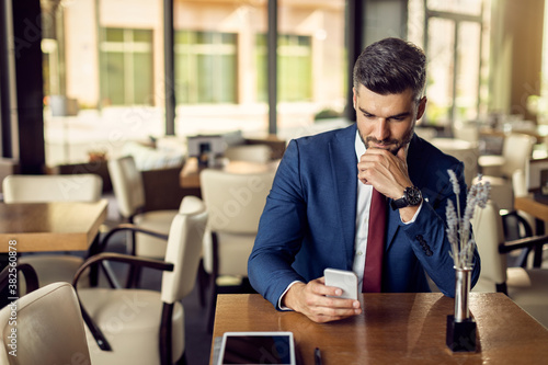 Male entrepreneur reading text message on mobile phone in a cafe. © Drazen