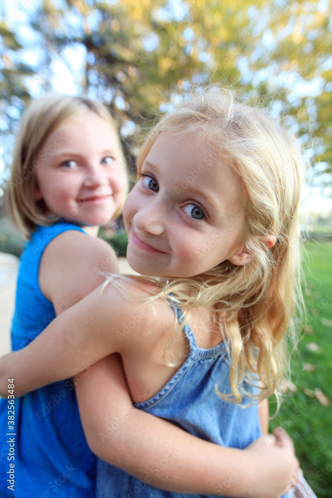 Sisters Hugging Wearing Blue One Looking Over Shoulder Sisters Hugging Wearing Blue One Looking Over Shoulder