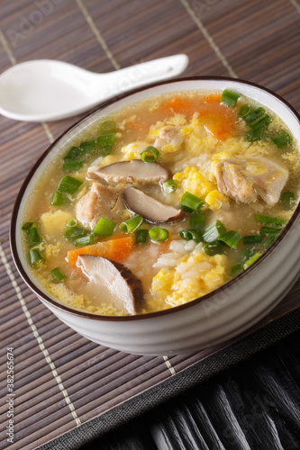 Zosui is a comforting Japanese rice soup cooked in a savory dashi broth with vegetables, eggs, mushrooms, and chicken close-up in a bowl on the table. Vertical