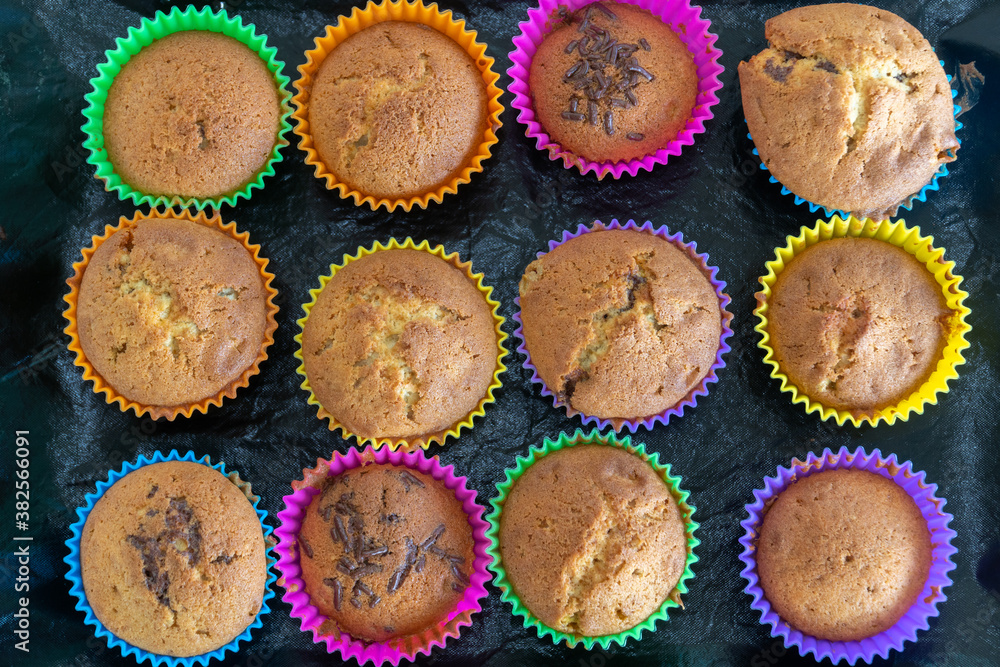 Delicious pastry cooked at home. Homemade cupcakes in multi-colored silicone molds and with colored chocolates inside on a baking tray.