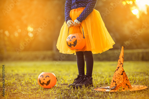 Halloween kids. Little girl with jack-o-lantern in witch hat with pumpkin candy bucket. Toddler kid in witch costume playing in autumn park. A Child in a carnival costume outdoors 