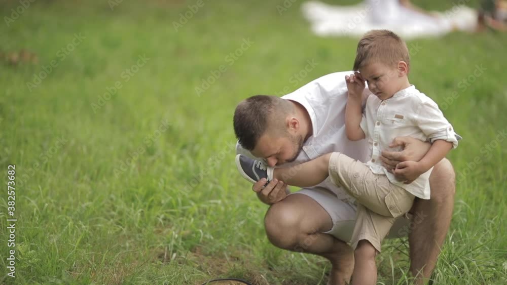 Caring young dark-haired bearded Caucasian father blowing at the bruised area on his little child leg. Fatherly love concept Caring young dark-haired bearded Caucasian father blowing at the bruised area on his little child leg. Fatherly love concept