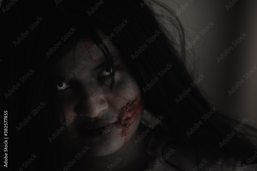 Female zombie in blood. Closeup face and eyes of Asian Woman ghost with blood. Horror creepy scary fear in a dark house. Hair covering the face, Halloween festival concept Female zombie in blood. Closeup face and eyes of Asian Woman ghost with blood. Horror creepy scary fear in a dark house. Hair covering the face, Halloween festival concept