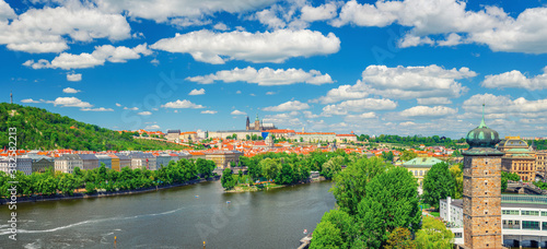 Panorama of Prague city historical centre with Prague Castle, St. Vitus Cathedral, Hradcany district, green hills and Vltava river, blue sky. Aerial panoramic view of Prague city, Czech Republic