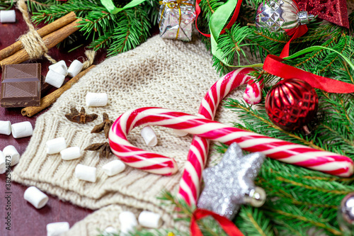 Bright Christmas and New Year celebration background with fir tree branches, holiday decorations and sweet red striped lollipops on light rustic backdrop with copy space.