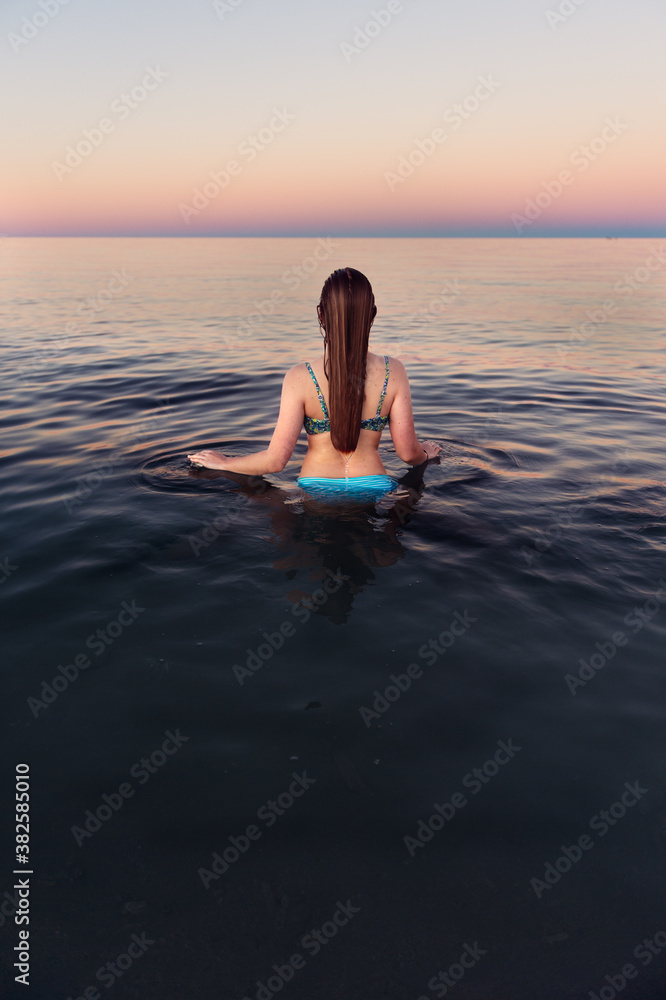 Girl viewed from behind standing in calm water at the beach at sunset Girl viewed from behind standing in calm water at the beach at sunset