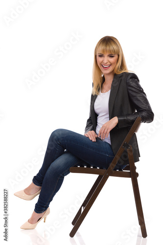 Laughing Woman Is Sitting On A Chair And Looking At Camera. Side View. © studioloco