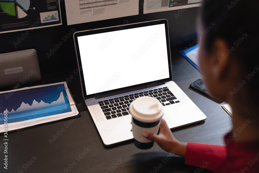 Woman holding coffee cup using laptop at office Woman holding coffee cup using laptop at office
