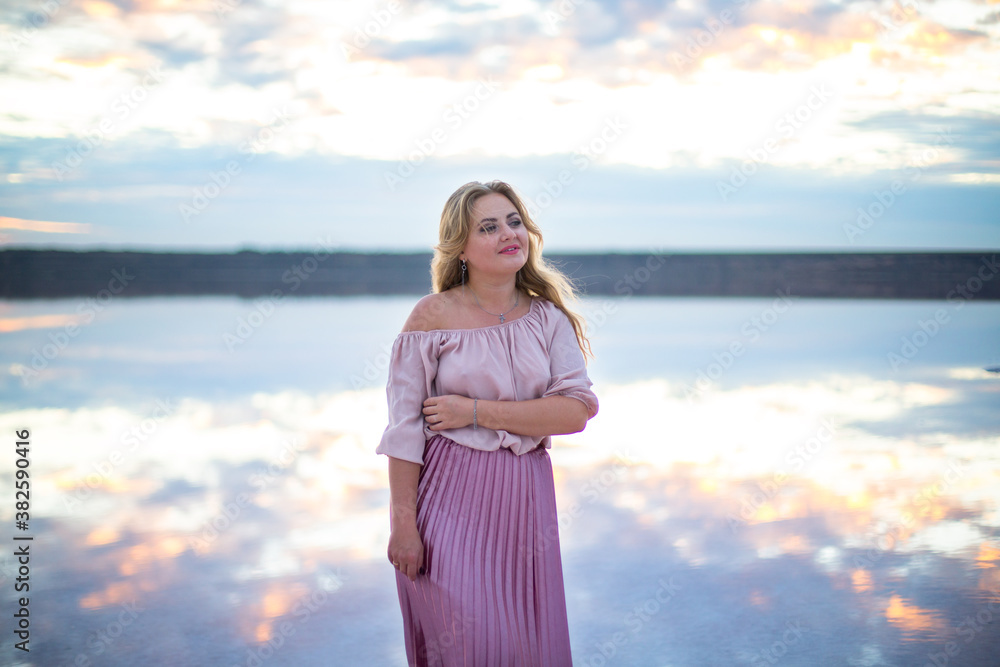 plump caucasian female in a pink dress on a pink salty still water lake at sunset plump caucasian female in a pink dress on a pink salty still water lake at sunset