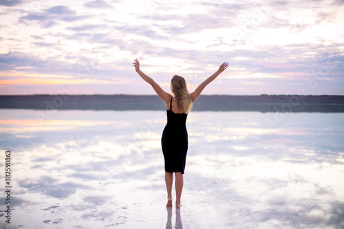 beautiful girl in a black dress on a salty pink lake at a vanilla sunset raised her hands