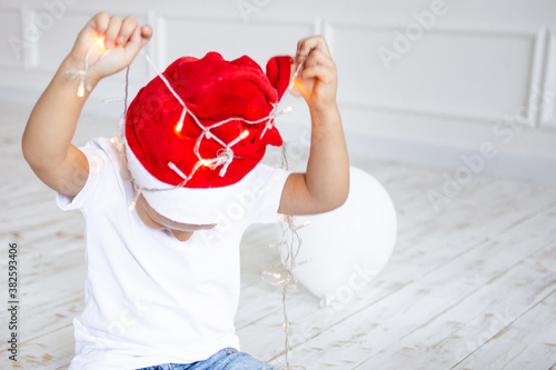 beautiful little child is celebrating Christmas. New Year's Holidays. Child in a Christmas hat with garlands in his hands