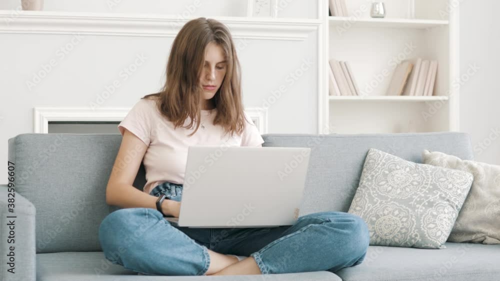 Young good looking Caucasian girl typing and working on the laptop computer as freelancer while sittng at home in the cozy white light living room. Stay, work and study from home Young good looking Caucasian girl typing and working on the laptop computer as freelancer while sittng at home in the cozy white light living room. Stay, work and study from home