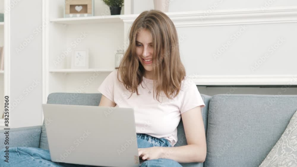 Smiling young woman sitting on couch using laptop notebook looking at screen typing message, happy lady chatting on computer browsing surfing internet social media studying or working online at home Smiling young woman sitting on couch using laptop notebook looking at screen typing message, happy lady chatting on computer browsing surfing internet social media studying or working online at home