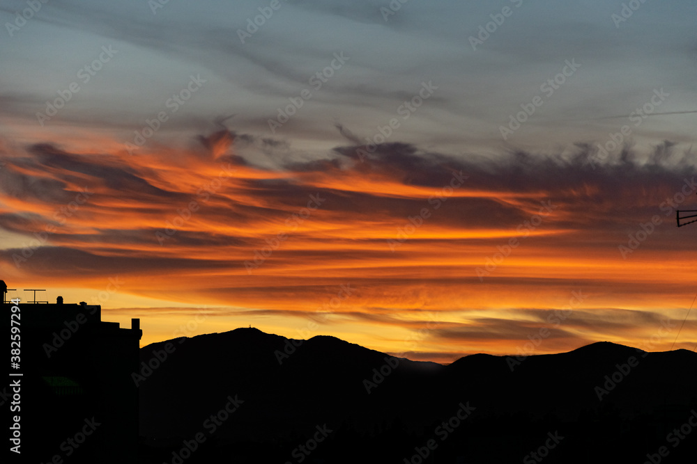 a close up of fire coloured clouds during a tropical sunset with a mountain range silhouette below