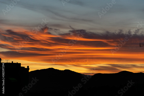 a close up of fire coloured clouds during a tropical sunset with a mountain range silhouette below