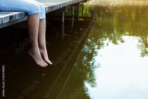 Fotografi Young woman sitting on a wooden jetty dangling her legs above the water