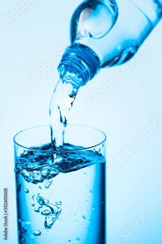 Pouring water from a bottle into glass on a blue background.