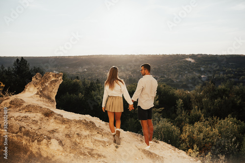 Beautiful stylish young couple in love walking in the summer on the mountain. They standing together on top of mountain. Lovely couple reached top of stone rock, feel happy see beautiful view. 