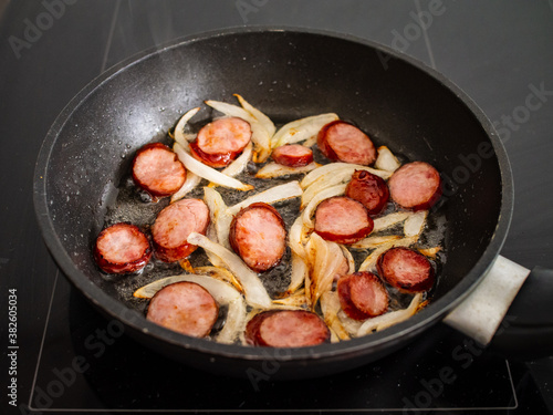 Frying sausage slices and white onion in pan 