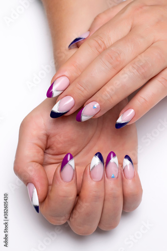 Colored French manicure on long sharp nails close-up on a white background. Gel design white  blue  purple and silver stripe and crystals.