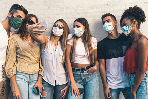  A multiracial group of young people have fun taking selfies with their smartphones together wearing the protective mask against the coronavirus. A concept of new behavioral habits and normality photo