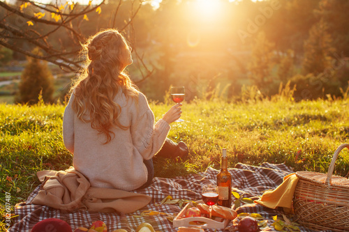 Girl Autumn Picnic. Perfect autumn warm day, autumn picnic in nature. girl sitting on a plaid with a wicker basket of products and a bottle of young red wine is enjoying the peace and sunshine  photo