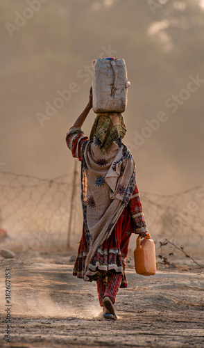water carrier woman with water pot on the head walking in the desert ,shepherds from Baluchistan , Pakistan 