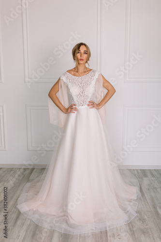 young woman in a white wedding dress with long hair before the engagement ceremony on a white background with a model appearance important wife for the bride posing in front of the photographer

