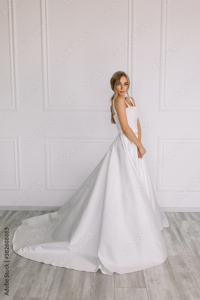 young woman in a white wedding dress with long hair before the engagement ceremony on a white background with a model appearance important wife for the bride posing in front of the photographer
