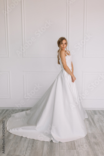 young woman in a white wedding dress with long hair before the engagement ceremony on a white background with a model appearance important wife for the bride posing in front of the photographer 
