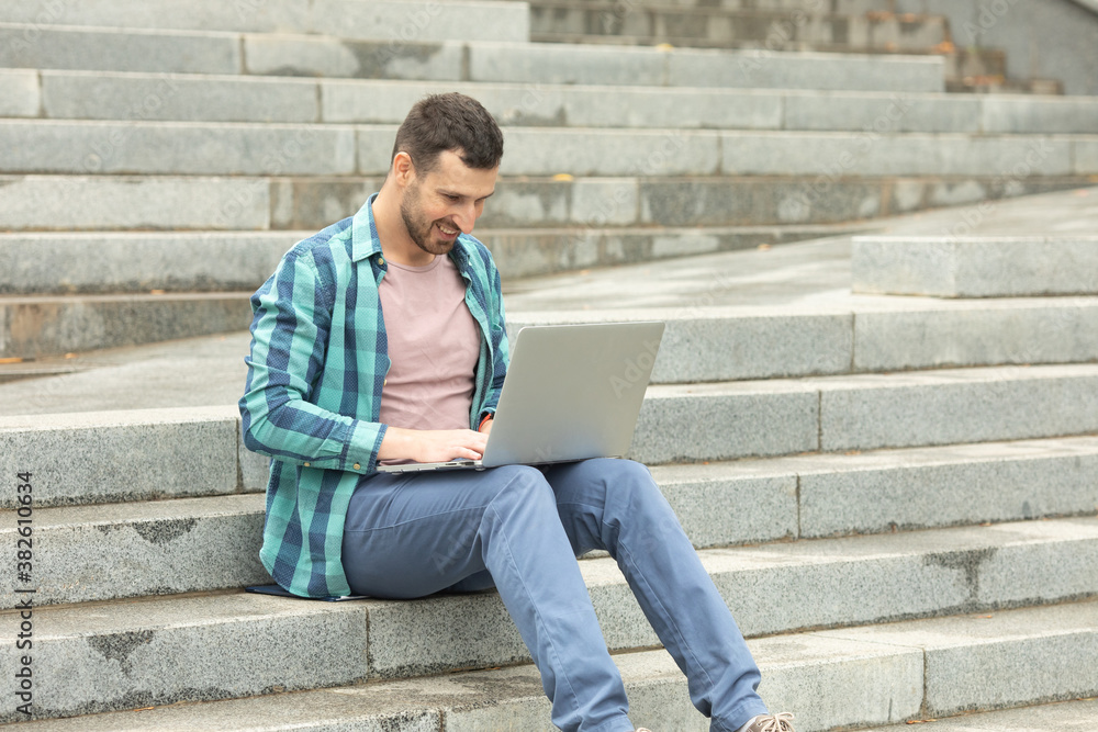 Young man freelancer is working outdoors on his computer laptop. He is sitting on the stone stairs. Working everywhere concept Young man freelancer is working outdoors on his computer laptop. He is sitting on the stone stairs. Working everywhere concept