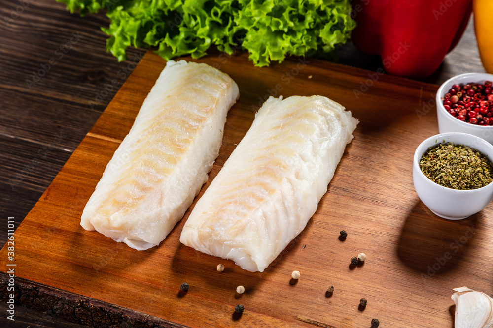 Fresh raw cod with seasonings and vegetables served on cutting board on wooden table
Fresh raw cod with seasonings and vegetables served on cutting board on wooden table