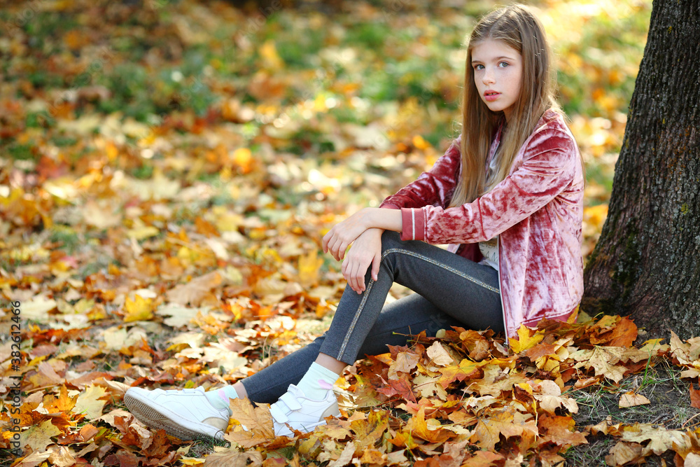girl is sitting near a big tree in the autumn park. girl is sitting near a big tree in the autumn park.