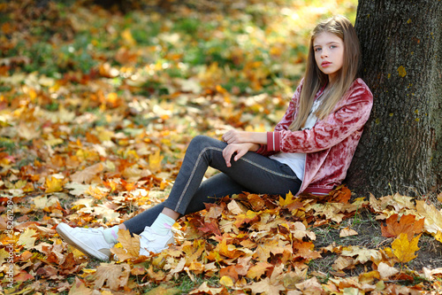 girl is sitting near a big tree in the autumn park.