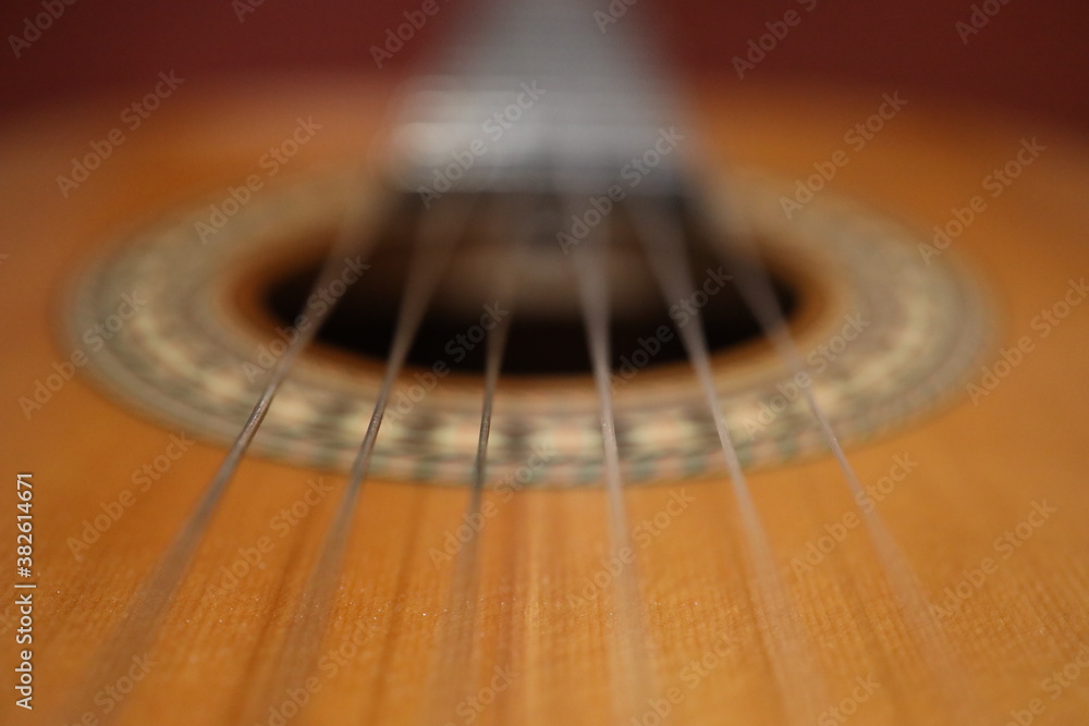 Fototapeta premium Saiten einer orangenen klassischen Gitarre mit einem schönverzierten Korpus aus der Nähe mit einem Marko Objektiv fotografiert. Es ist ein roter Hintergrund zu sehen.