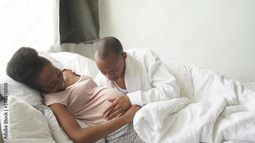 Black husband cuddling pregnant wife on bed, touch her belly. Happy relationships, pregnancy concept. Black husband cuddling pregnant wife on bed, touch her belly. Happy relationships, pregnancy concept.