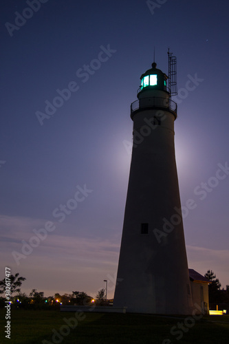 Illuminated Lighthouse Silhouette At Night. Illuminated beacon of the Fort Gratiot Lighthouse in Port Huron, Michigan. Vertical orientation and back lit by moonlight.