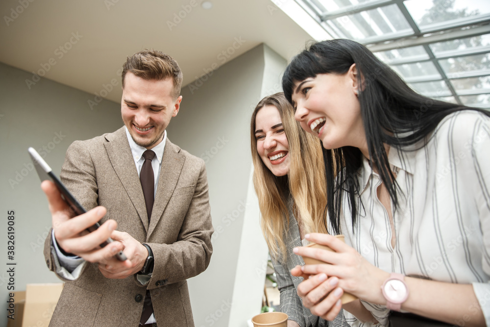 A guy is showing something on his tablet to a two girls. They are laughing together A guy is showing something on his tablet to a two girls. They are laughing together