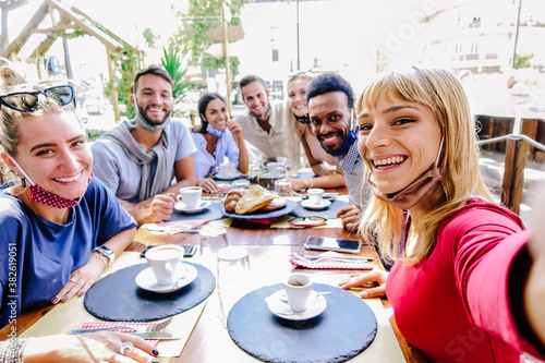 Multiracial group of friends wearing protection mask at the restaurant. Happy people celebrating having fan at coffee shop. New normal concept.