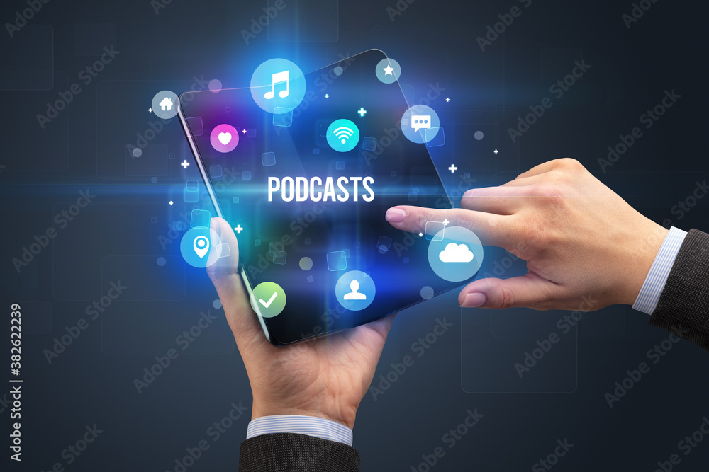 Businessman holding a foldable smartphone with PODCASTS inscription, social media concept Businessman holding a foldable smartphone with PODCASTS inscription, social media concept