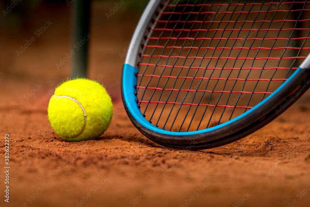 Tennis racket and ball on a clay court.