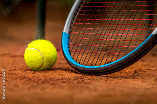 Tennis racket and ball on a clay court.