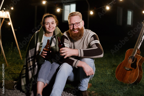 Couple have a good time together on night picnic drinking beverage from bottles
