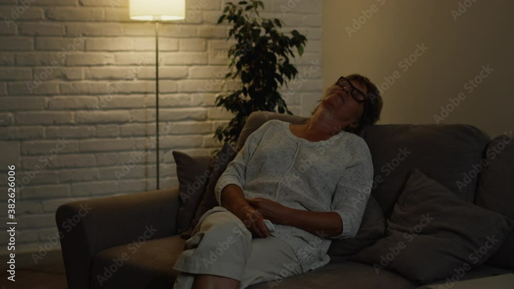 Beautiful Middle Aged Woman Sitting On The Couch In Her Apartment. She Turns Off The TV And Throws Her Head On The Back Of The Sofa. Beautiful Middle Aged Woman Sitting On The Couch In Her Apartment. She Turns Off The TV And Throws Her Head On The Back Of The Sofa.