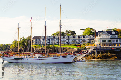 Luxurious and elegant Victorian architecture New England wooden cottage resort or hotel in Bar Harbor, Maine with beautiful sailing yacht or windjammer on sunny morning photo