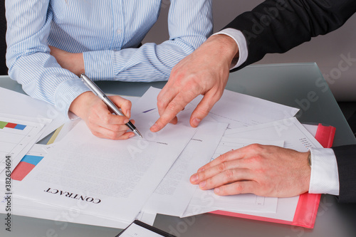 Business woman sitting at table and signing documents at office. Businessman pointing finger at the document and showing to the customer where to sign a contract.