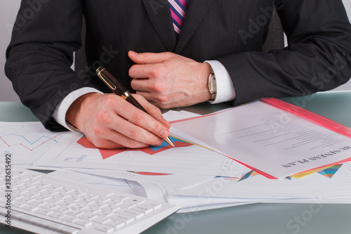 Close up male accountant working with financial documents. Businessman compiling and analysing financial information sitting at office table.