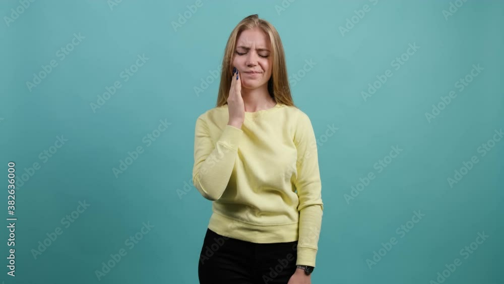 Young woman isolated on turquoise background suffering from severe toothache, feeling pain, she is pressing fingers to cheek to calm it down. Young woman isolated on turquoise background suffering from severe toothache, feeling pain, she is pressing fingers to cheek to calm it down.