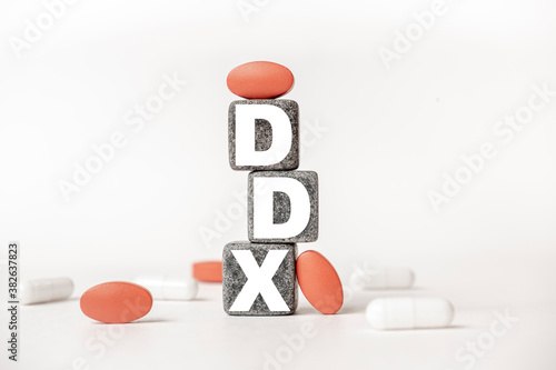 a group of white and red pills and cubes with the word DDX Differential diagnosis on them, white background. Concept carehealth, treatment, therapy. photo